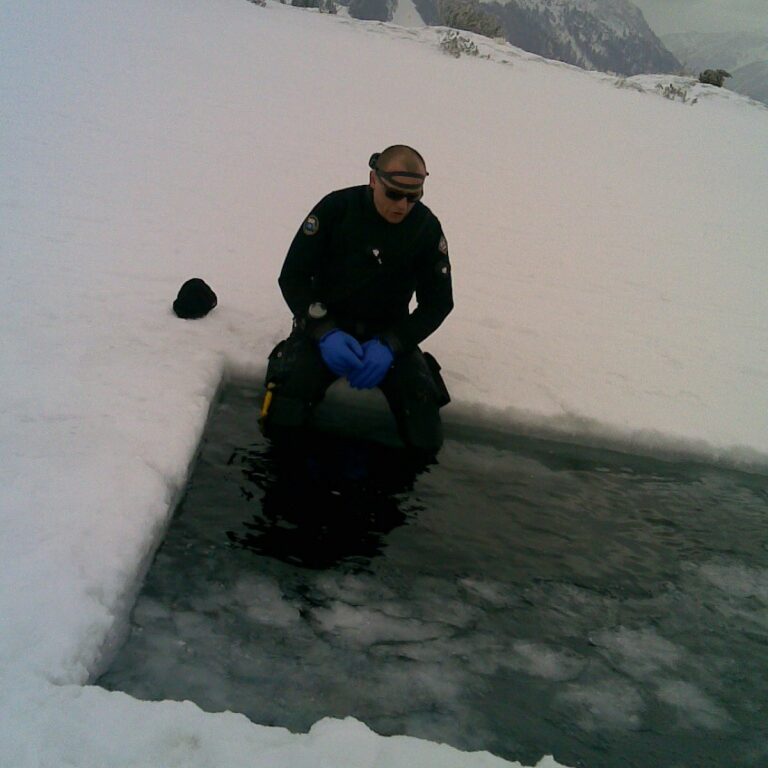 Taucher im Trockentauchanzug am Eis sitzend